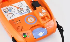 Pomarańczowy AED gotowy do użycia. Schemat pokazuje, jak prawidłowo umieścić elektrody do defibrylacji.