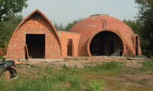 Dwa budynki z cegły, jeden z łukowatym dachem, drugi z okrągłą kopułą, w trakcie budowy.