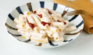 Piatto di pasta cremosa con pesto, pomodori secchi e ricotta. Un gusto mediterraneo in ogni boccone.