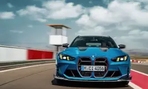 Niebieskie BMW M3 Touring pędzi po torze wyścigowym, chmury na niebie dodają dynamiki.
