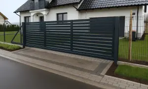 Nowoczesna, ciemnoszara brama przesuwna zapewnia odpowiednią szerokość bramy wjazdowej dla tira, prowadząc do posesji z białym domem.
