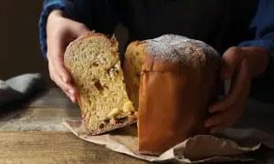 Puszysta babka drożdżowa włoska, z rodzynkami i kandyzowanymi owocami, posypana cukrem pudrem, prezentowana na drewnianym stole.