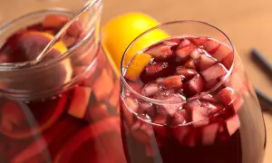 Un bicchiere e una caraffa pieni di vino per sangria, con pezzi di frutta e fette d'arancia.