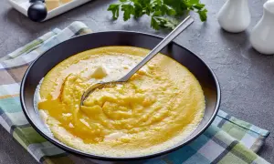 Cremige Polenta mit Butter in einer schwarzen Schüssel, bereit für ein köstliches polenta rezept. Ein Löffel ruht darin.