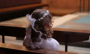 Dziewczynka w białej sukience i wianku na głowie siedzi w kościele. Czy nie przyjęcie komunii jest grzechem?