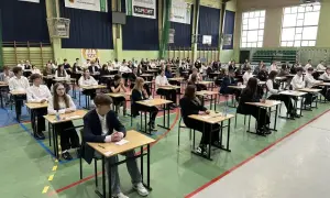 Uczniowie siedzą przy ławkach w sali gimnastycznej, czekając na wyniki egzaminu ósmoklasisty.