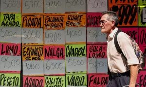 Starszy mężczyzna mija kolorowe tablice z cenami mięsa, gdzie widnieje m.in. peso argentyńskie.