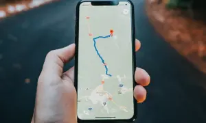 Dłoń trzyma iPhone'a z mapą Google, pokazującą trasę i lokalizację.