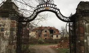 Zrujnowany pałac w glince, zniszczona brama i dziki ogród.