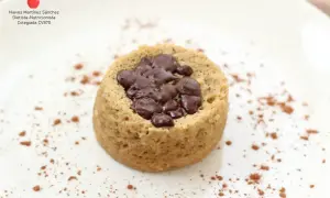 Delicioso mug cake saludable con trozos de chocolate negro, espolvoreado con cacao en polvo sobre un plato blanco.