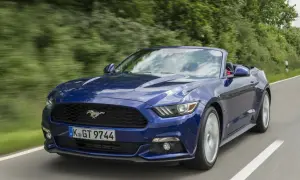 Błękitny mustang cabrio pędzi po krętej drodze wśród zieleni.