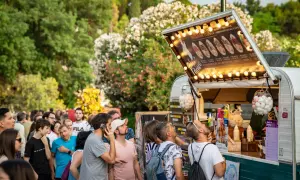 Gente disfrutando de food trucks en Zaragoza, un evento donde la gastronomía florece entre árboles y flores.
