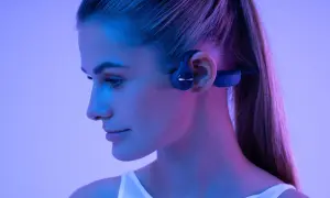 Profil d'une femme portant un casque à conduction osseuse bleu, éclairée par des lumières bleues et roses.