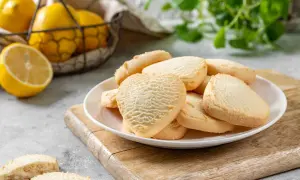 Deliziosi biscotti senza burro a forma di cuore e rotondi, serviti su un piatto bianco con limoni freschi sullo sfondo.
