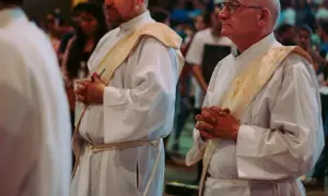 Diakoni i księża w białych szatach, z modlitewnie złożonymi dłońmi. Różnica między diakonem stałym a księdzem, ich obowiązki i przywileje.