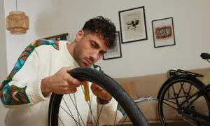 Mężczyzna w kolorowym swetrze naprawia rower, wyjmując detkę.