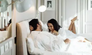 Ett lyckligt par i morgonrockar skrattar i en lyxig säng, kanske på ett hotell i St. Gallen.