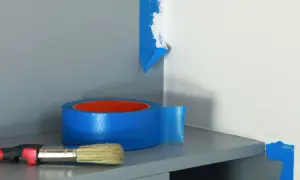 Rouleau de ruban bleu et pinceau prêts à repeindre une partie de mur.