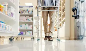 Mężczyzna z balkonikiem w aptece. Świadczenie wspierające wyrównanie szans w dostępie do leków i sprzętu medycznego.