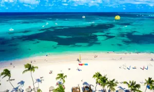 Rajska plaża z palmami i turkusową wodą. Wiele łodzi, parasailing i ludzie cieszący się słońcem. Dominikana ceny wakacji zachęcają do odpoczynku.