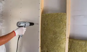 Instalación de aislamiento para como aislar una pared del ruido de los vecinos. Se atornilla placa de yeso sobre estructura de madera con lana mineral.