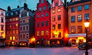 Färgstarka hus i **altstadt Stockholm** lyser upp en kullerstensbelagd gata i skymningen.