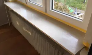 Un nouveau rebord de fenêtre en pierre, prêt à accueillir des plantes, surplombe un radiateur blanc.