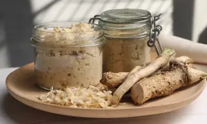 Jak zrobić chrzan domowy do słoików? Na talerzu świeży chrzan, tarta masa i dwa słoiki gotowego produktu.