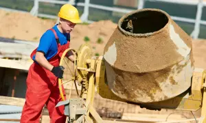 Robotnik w żółtym kasku i czerwonym ogrodniczkach obsługuje betoniarkę. Kluczowe są tu beton bez żwiru proporcje.