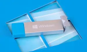 Srebrny pendrive startowy Windows 10 z niebieską nakładką, leżący na niebieskim tle z logo Windows.