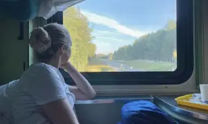 Frau blickt aus dem Fenster eines Nachtzuges nach Italien. Die Landschaft zieht vorbei, Bäume und eine Straße sind zu sehen.