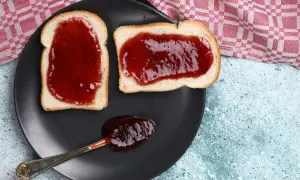 Zwei Scheiben Toast mit leckerer Jostabeeremarmelade und ein Löffel voll davon auf einem schwarzen Teller.