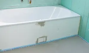 Einbau einer neuen, weißen Badewanne in einem Badezimmer im Rohbau. Grüne Gipskartonplatten und vorbereitete Rohre sind sichtbar.