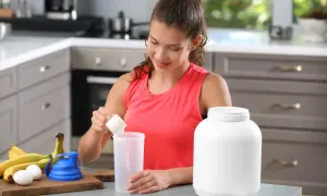 Donna prepara un frullato con proteine prima o dopo allenamento, con banane e uova sul bancone.