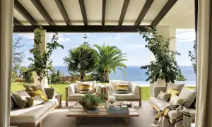 Cómodos porches de entrada principal con sofás de madera, cojines y mantas, con vistas al mar y palmeras.