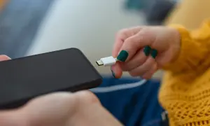 Dłoń z zielonymi paznokciami próbuje podłączyć kabel do telefonu, ale telefon się nie ładuje.