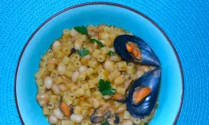 Piatto di pasta fagioli e cozze, un classico della cucina italiana, servito in una ciotola azzurra su un tovagliolo blu.