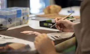 Une main tient un pinceau, peignant un visage sur du papier brun. La scène illustre comment devenir artiste, avec des fournitures d'art en arrière-plan.