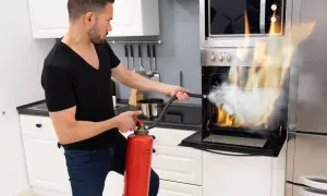 Mężczyzna gasi płonący piekarnik gaśnicą. Warto wiedzieć, jaka gaśnica do domu, by uniknąć takich sytuacji.