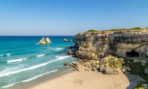 Scogliere calcaree e mare turchese, un paradiso tra le località balneari puglia. Faraglioni emergono dall'acqua cristallina, mentre una grotta si apre nella roccia.