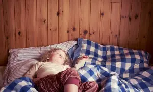 En 3-åring sover i en säng med rutiga täcken. Det är vanligt att en 3-åring kissar på sig på natten.