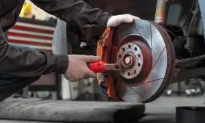 Mechanik w rękawiczkach dokonuje wymiany klocków hamulcowych, używając klucza do odkręcenia śruby zacisku.