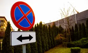 Znak zakazu zatrzymywania się i postoju, z tabliczką wskazującą kierunki. Uważaj, bo grozi za to mandat.