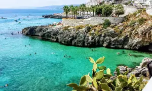 Scogliera con mare cristallino e gente che nuota, tipica dei paesi sul mare in Puglia.