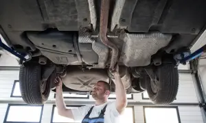 Mechanik sprawdza podwozie sedana na podnośniku, badając układ wydechowy i zawieszenie.