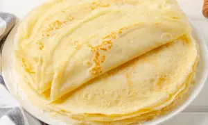 Stos puszystych, złotych naleśników bez jajek, ułożonych na białym talerzu. Idealne na śniadanie lub deser.