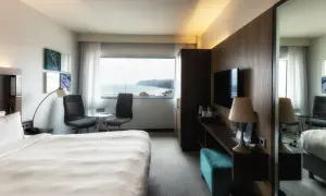 Pokój w hotelu Marriott Gdynia z widokiem na morze. Wygodne łóżko, stolik z krzesłami i telewizor.
