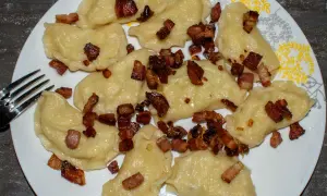 Pyszne pierogi galicyjskie z chrupiącym boczkiem na talerzu. Obok leży widelec.