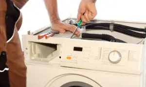 Naprawa pralki, która nie pobiera wody. Technik dokręca śrubę śrubokrętem.