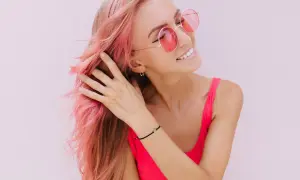 Ragazza con capelli rosa sfumati, occhiali da sole rotondi e un top fucsia. Il suo shampoo colorante mantiene vibrante la chioma.